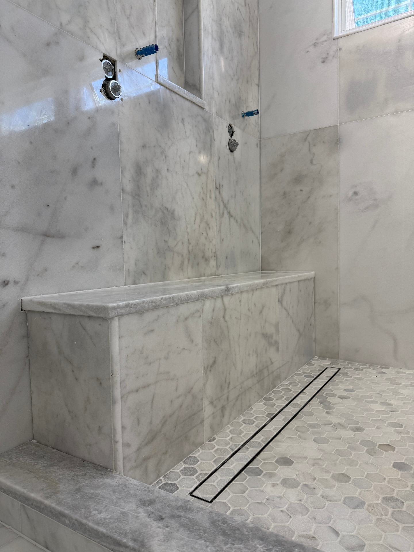 Finished marble shower with built-in bench, linear drain, and hex mosaic floor